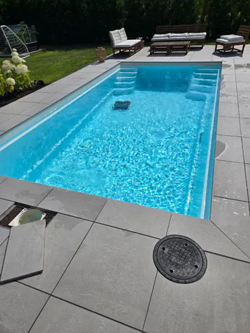 Färdig glasfiberpool med grå plattor och poolrobot